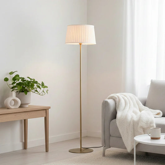 Modern gold floor lamp with pleated white fabric shade styled in a minimal living room setting beside sofa or armchair.