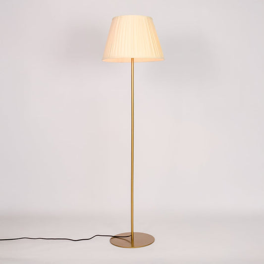 Gold metal floor lamp glowing warmly through pleated cream fabric shade on white background for cozy home Decor.
