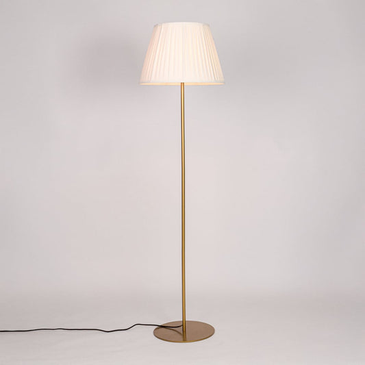 Gold metal floor lamp glowing warmly through pleated white fabric shade on white background for cozy home Decor.