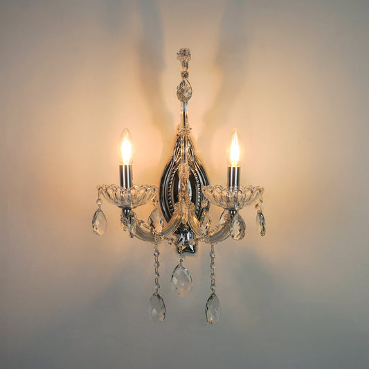 A classic three-light wall sconce with a polished silver-tone metal frame and clear crystal teardrop pendants, shown illuminated against a neutral wall.