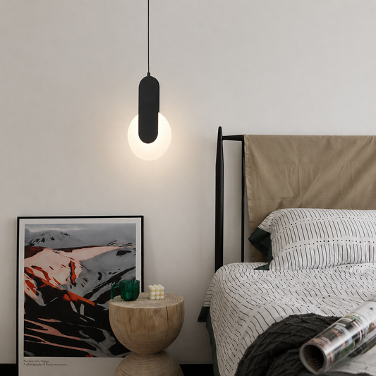 A modern black pendant light with a glowing white globe bulb hanging in a minimalist bedroom next to a bed with white and black striped bedding.