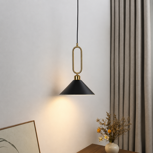 A modern pendant light with a black conical shade and a gold-toned oval frame, hanging in a styled room next to a gray curtain with warm light glowing from the lamp.