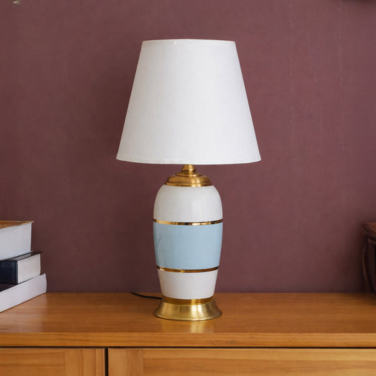 Table lamp with white and gold ceramic base and white shade on wooden table warm ambient lighting for living room decor.