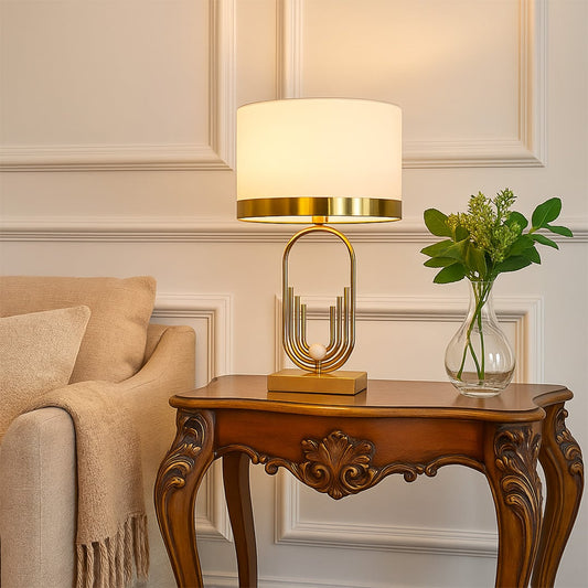 White fabric lamp on carved console table with light on and beige sofa background for classic warm décor.