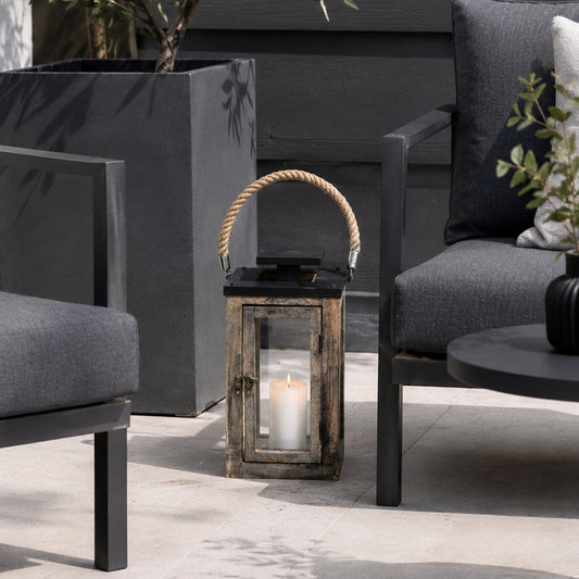 Decorative lantern with a candle on a patio with chairs and plants.