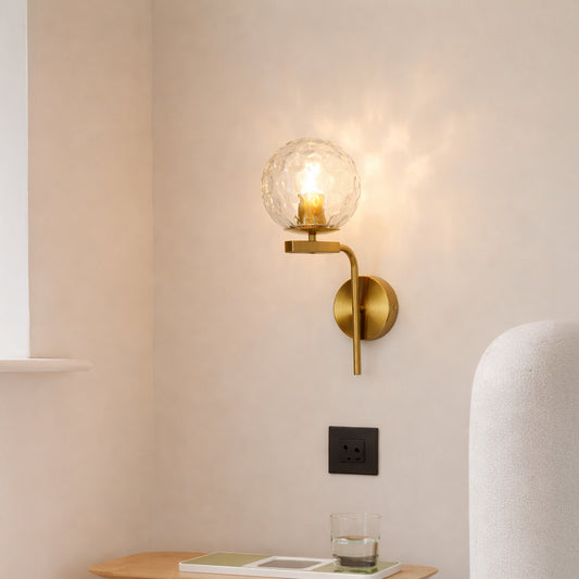 Modern gold metal wall light with textured glass globe for elegant bedroom and luxury decor styling spaces.