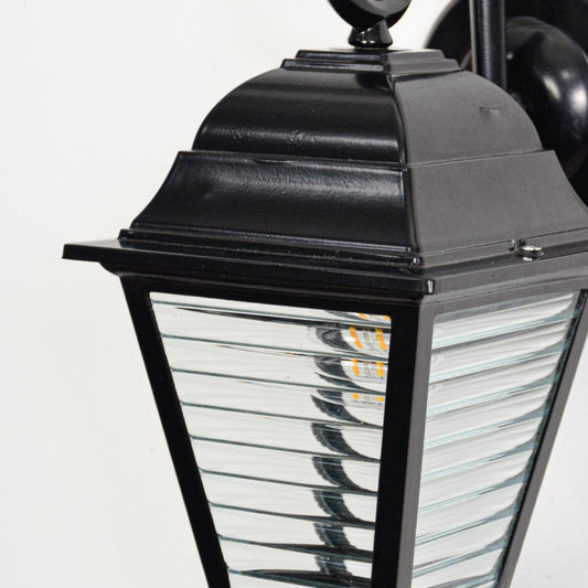 Closeup of black metal wall lantern showcasing ribbed clear glass panels sturdy frame and vintage outdoor styling.