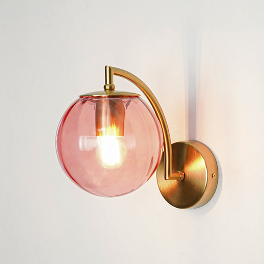 Stylish pink glass wall light with curved gold metal arm mounted on clean white background perfect for modern bedroom or living space lighting.