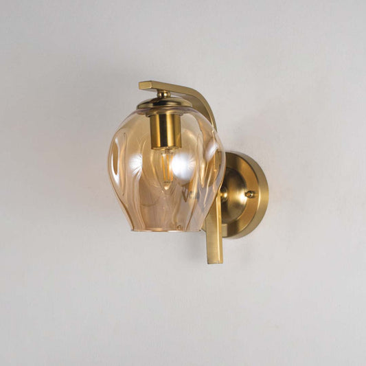 Gold wall sconce with sculpted glass shade and light off displayed on a white background showing the detailing of the fixture without illumination.