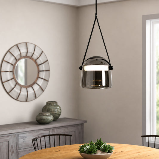 A modern pendant light with a brushed silver dome shade and black hanging straps, suspended over a wooden dining table in a neutral-toned dining room.