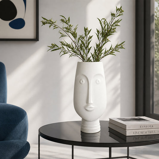 White ceramic face flower vase with green stems placed on side table for modern home decor styling.