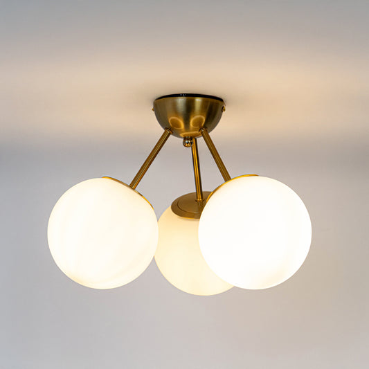 Modern gold metal ceiling light with three white glass globes for elegant bedroom and premium interior decor spaces.
