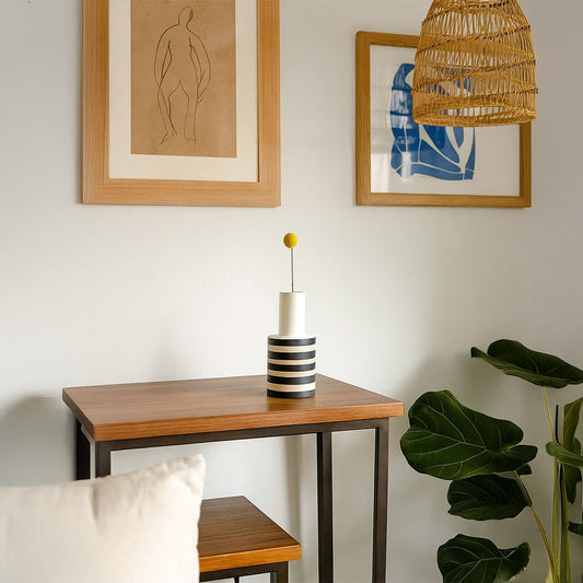 Modern black and white striped ceramic vase styled on a wooden console table with framed artwork and a natural woven pendant lamp for contemporary home decor inspiration.