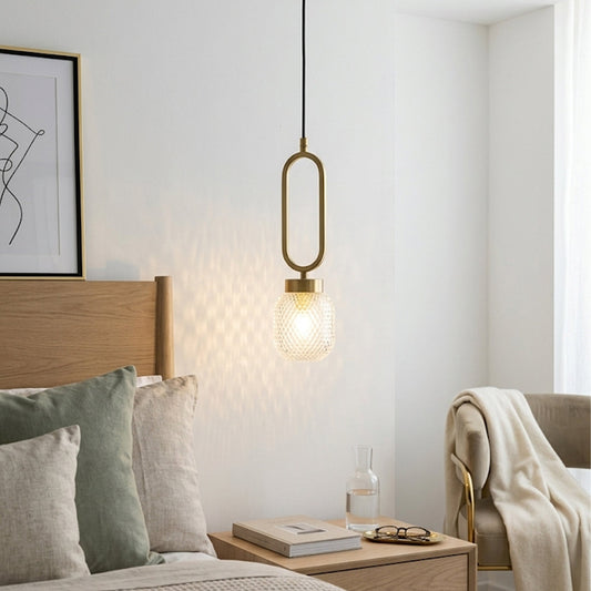 Minimal gold pendant light with oval frame and glass bulb hanging beside bed in soft neutral bedroom setting perfect for warm ambient lighting.