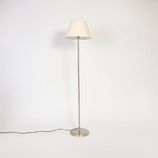 Steel floor lamp with cream pleated fabric shade switched off on plain white background home lighting accent.