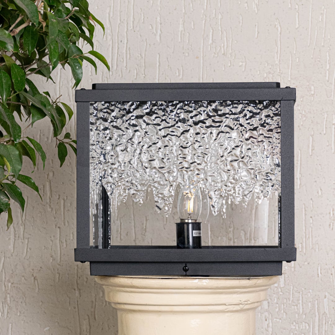 Modern pillar light with black frame and rippled glass body displayed off on clean white background surface.