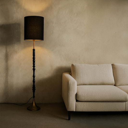Black floor lamp with fabric shade creating warm ambient lighting beside sofa in a sophisticated living room.