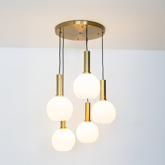 Warm glowing white globe pendant lights with gold holders arranged in a five light cluster displayed on a bright white background for decor styling.