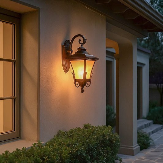A classic outdoor wall lantern light glowing warmly at the entrance of a home with soft illumination cast on the wall and surrounding greenery during evening time.