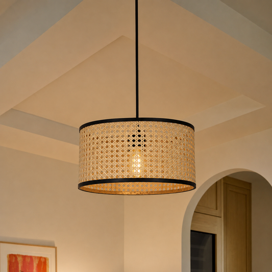 A cylindrical pendant light with a natural woven rattan shade and black metal trim, hanging in a warm, modern interior setting.