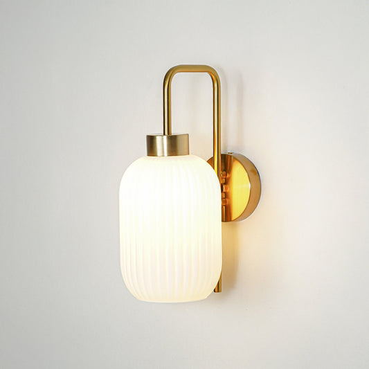 Gold finish wall light with white ribbed glass shade emitting soft warm glow ideal for bedroom or hallway wall decor placement.