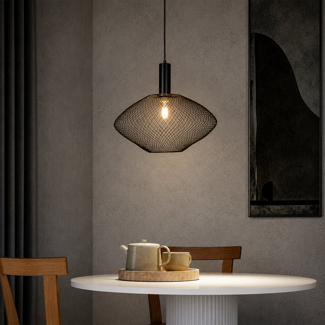 A modern pendant light with a black metal mesh dome shade hangs over a round white dining table in a minimalist room with textured gray walls and wooden chairs.