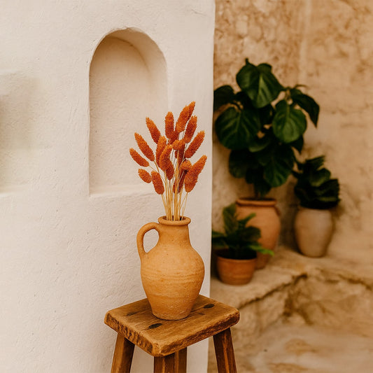 Rust orange dried bunny tail stems arranged in a rustic terracotta vase on a wooden stool creating a warm earthy lifestyle decor accent for cozy interior spaces.