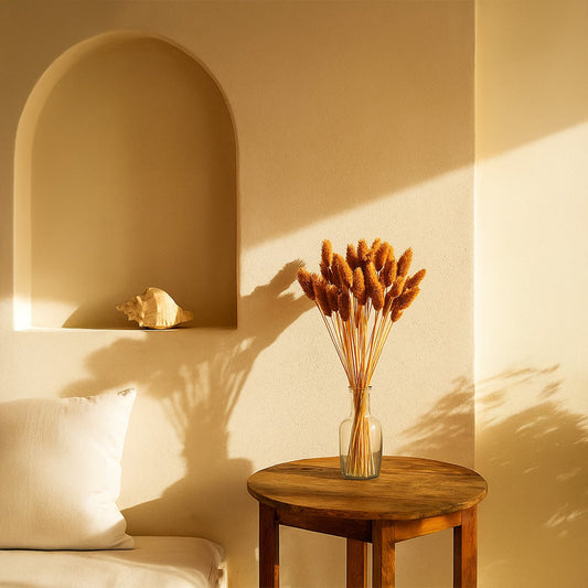 Warm brown dried bunny tail stems arranged in a clear glass vase on a wooden table creating a soft natural lifestyle decor accent in a sunlit cozy interior.