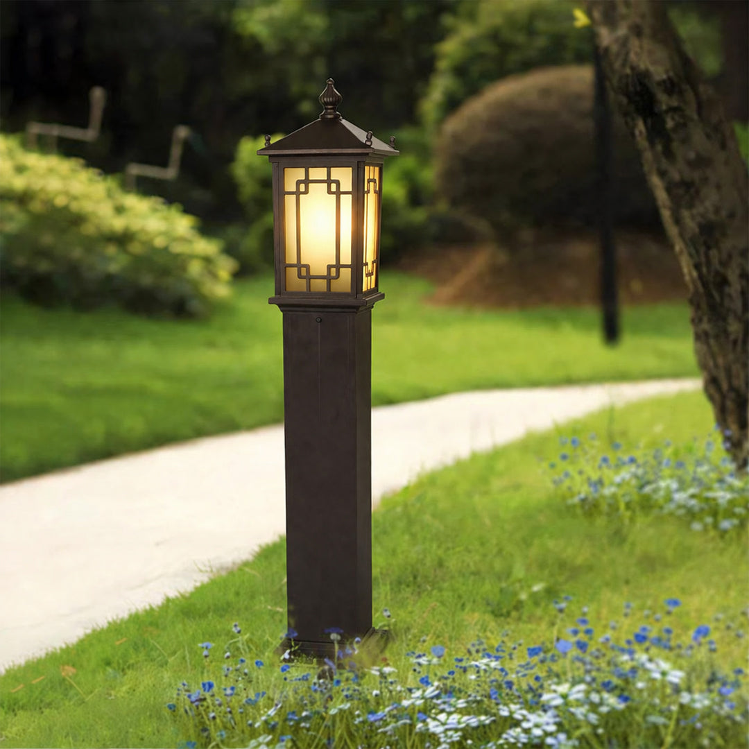 Outdoor pathway light with warm glowing lantern installed along garden path with greenery creating ambient landscape lighting.