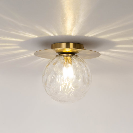 Modern gold metal ceiling light with textured glass shade casting decorative light patterns for luxury decor spaces.