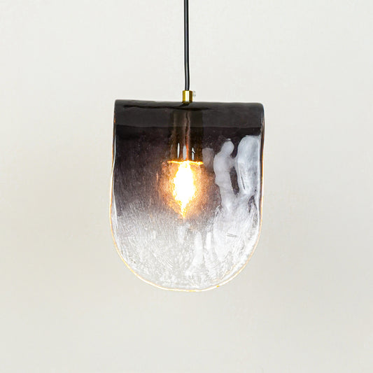 Frosted textured glass pendant light with glowing bulb and hanging cord placed against neutral wall background showcasing stylish modern lighting design.