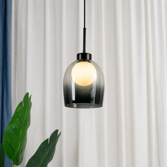 A modern pendant light with a black metal rod and a dark-to-clear gradient glass shade, glowing with a warm light in front of white curtains and a blue curtain panel on the left.