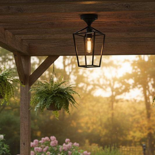 Black metal outdoor ceiling light with clear glass shade glowing warmly under a wooden pergola creating a cozy garden seating ambience at sunset.