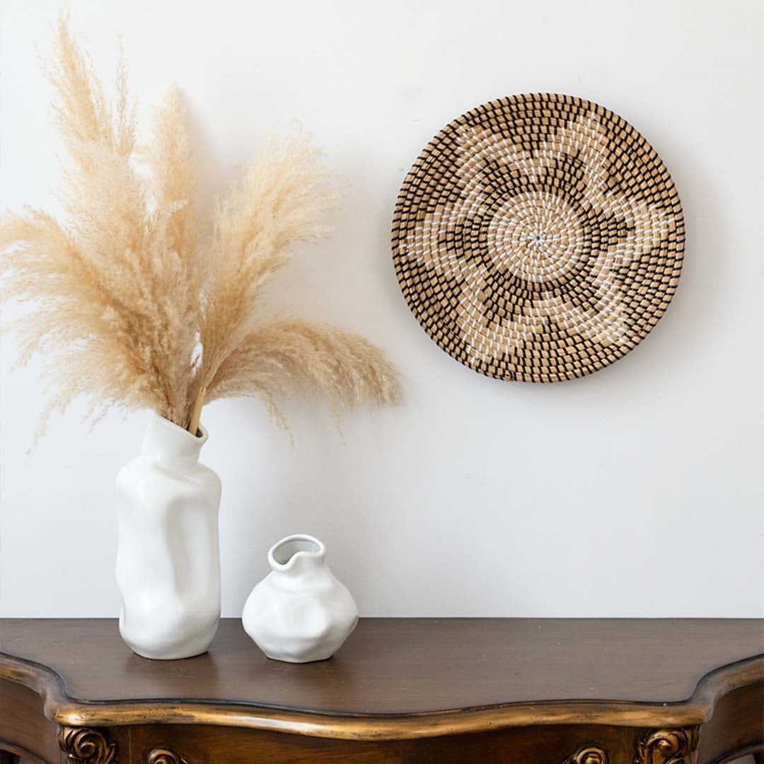 Handwoven wicker basket wall decor styled with pampas grass in vase on wooden console for modern boho home interiors.