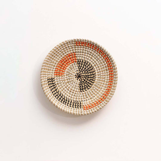 Round natural woven seagrass basket with orange and black geometric pattern for modern bohemian home wall art display.