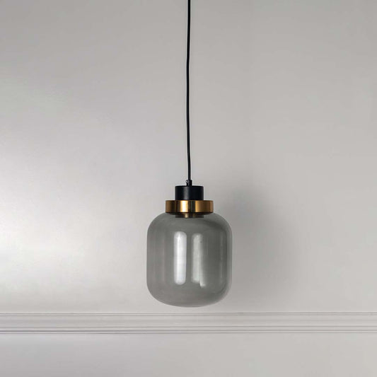 Smoky glass pendant light with black and gold fixture hanging against white background showcasing modern decorative lighting aesthetic.