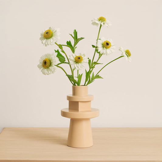 Modern beige ceramic geometric vase holding white daisy flowers on a light wooden table for minimalist Scandinavian home decor styling.
