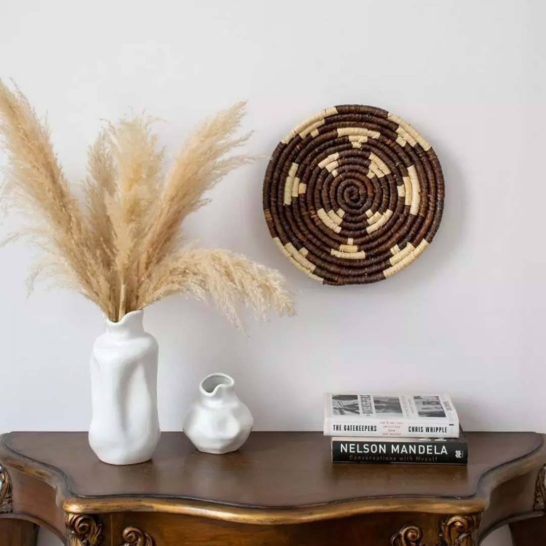 Handwoven seagrass wall basket decor in natural beige and dark brown displayed above a console creating boho home style.