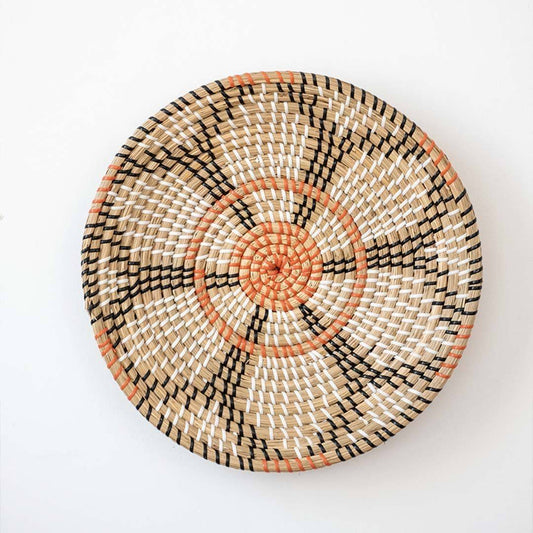 Beautiful orange and black floral patterned woven seagrass wall basket plate decoration isolated on a white backdrop.
