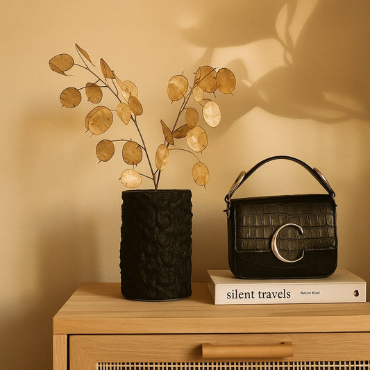 Black cylindrical textured ceramic vase styled with a single white flower displayed on a marble console in an elegant interior.