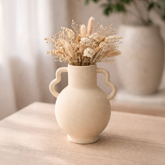 Beige ceramic double handle vase with dried stems placed on wooden table adding warm rustic charm to living room decor.
