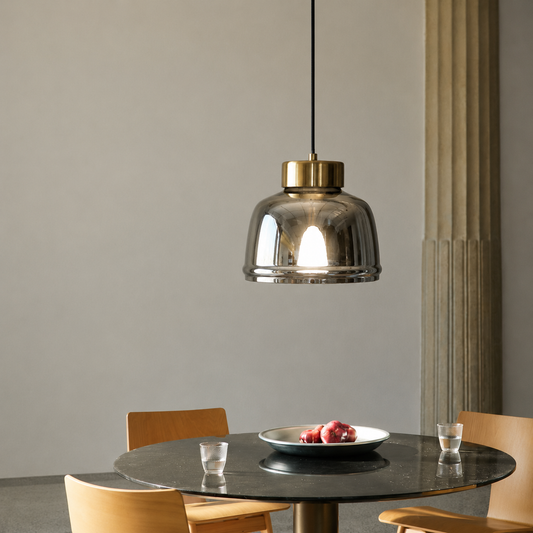 A modern pendant light with a smoked glass dome and brass cap hanging over a round black dining table with wooden chairs.