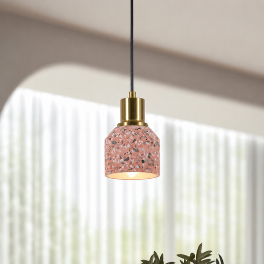 A modern pendant light with a terrazzo-patterned pink glass shade, a brass-finished metal collar, and a black hanging cord, shown in a softly lit interior setting.
