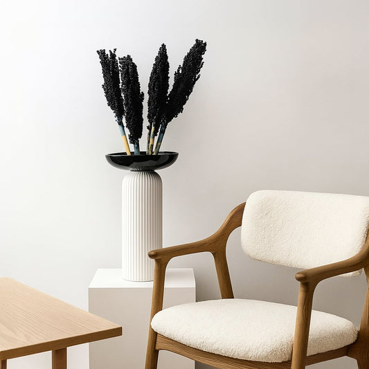Modern decorative vase with ribbed white ceramic base and black dried florals placed beside wooden chair for minimalist living room decor.