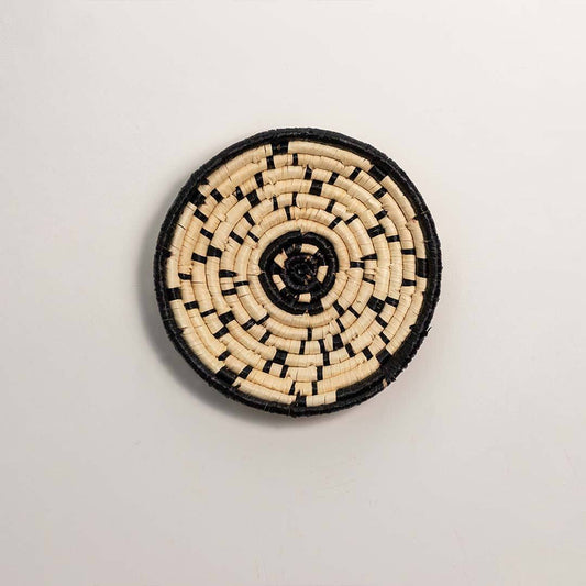 Round woven black and cream seagrass wall basket with geometric abstract dotted line pattern on white background image.