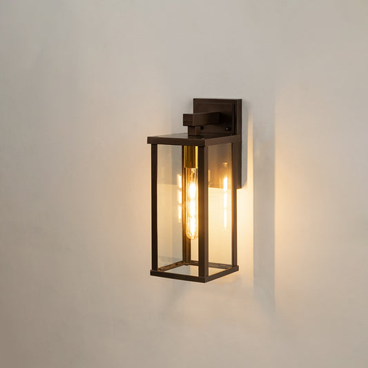 Modern black rectangular outdoor wall light on white background with clear glass panels illuminating a warm vintage glow.