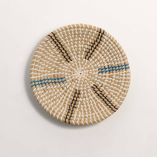 Round handcrafted natural cream seagrass wall basket with blue and grey radial spoke patterns on white background.