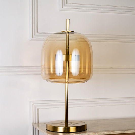 Gold metal table lamp with amber glass shade shown switched off on white background for minimal stylish decor.