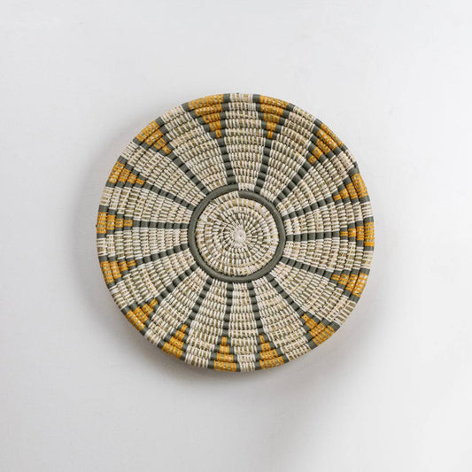 Round handcrafted seagrass wall basket with white grey and mustard pattern for home décor on white background image.