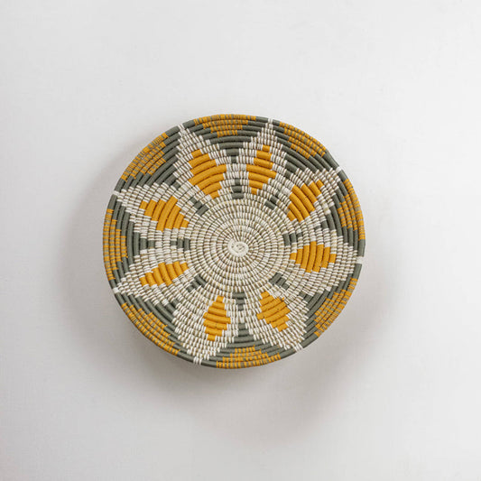 Round handcrafted seagrass wall basket with white and mustard pattern for boho home décor on white background image.
